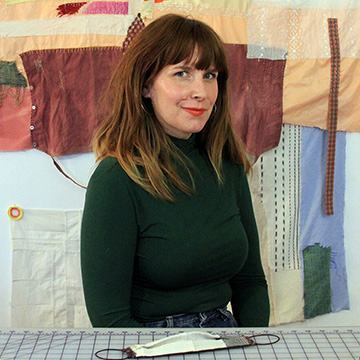 Hadley Clark sitting in front of a mended blanket that is hanging on the wall behind her