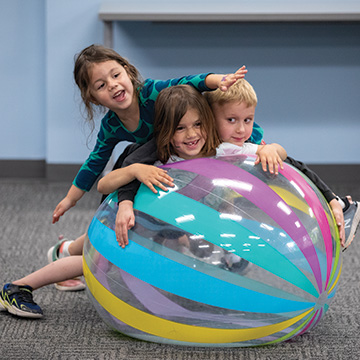 three small children playing with a large inflatable ball