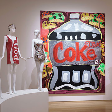 a large painting of a coke bottle hangs on the gallery wall next to the main signage for A Match Made in Heaven exhibition at the Nerman Museum