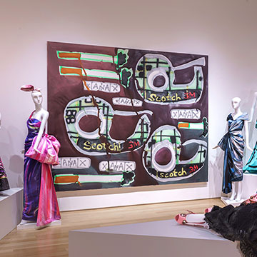 a large painting of scotch tape dispensers by Katherine Bernhardt hangs on the gallery wall next to the main signage for A Match Made in Heaven exhibition at the Nerman Museum